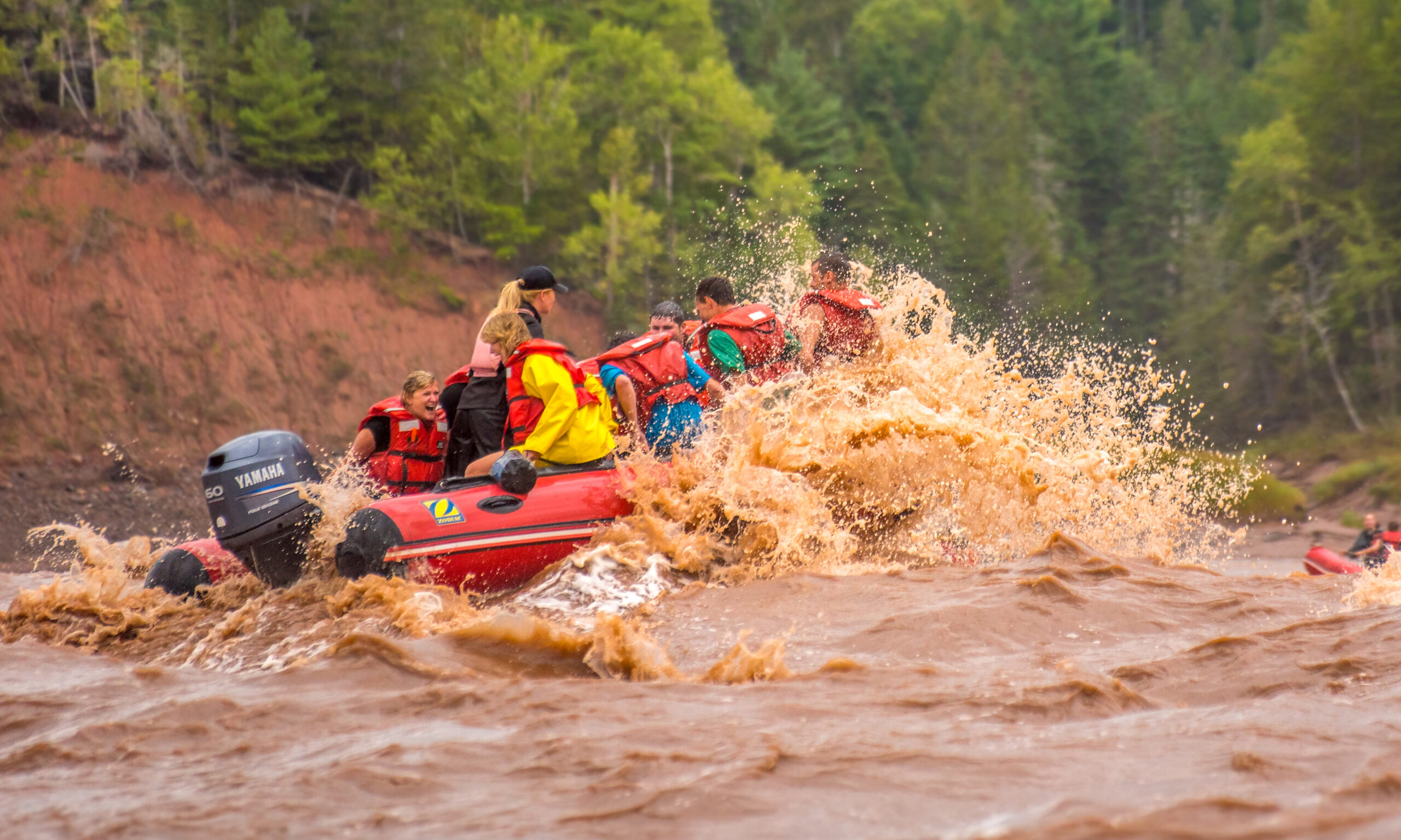 A zodiac rafting carrying passengers navigates through a large wave during a tidal bore rafting tour, soaking everyone on board.