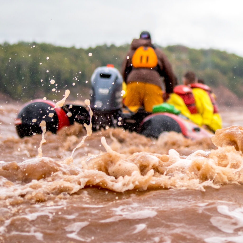 A zodiac boat carrying passengers travels down the Shubenacadie River for tidal bore rafting.