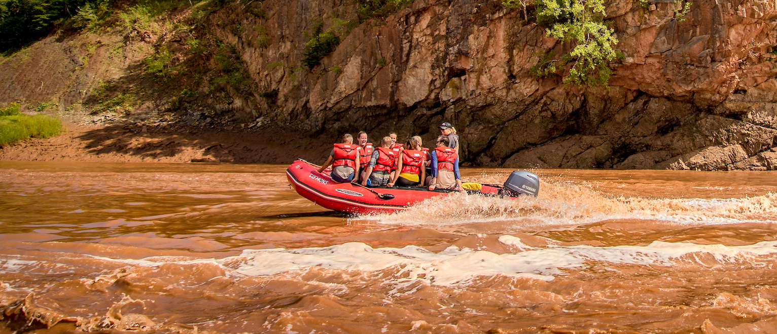 A zodiac boat carrying passengers travels down the Shubenacadie River for tidal bore rafting.