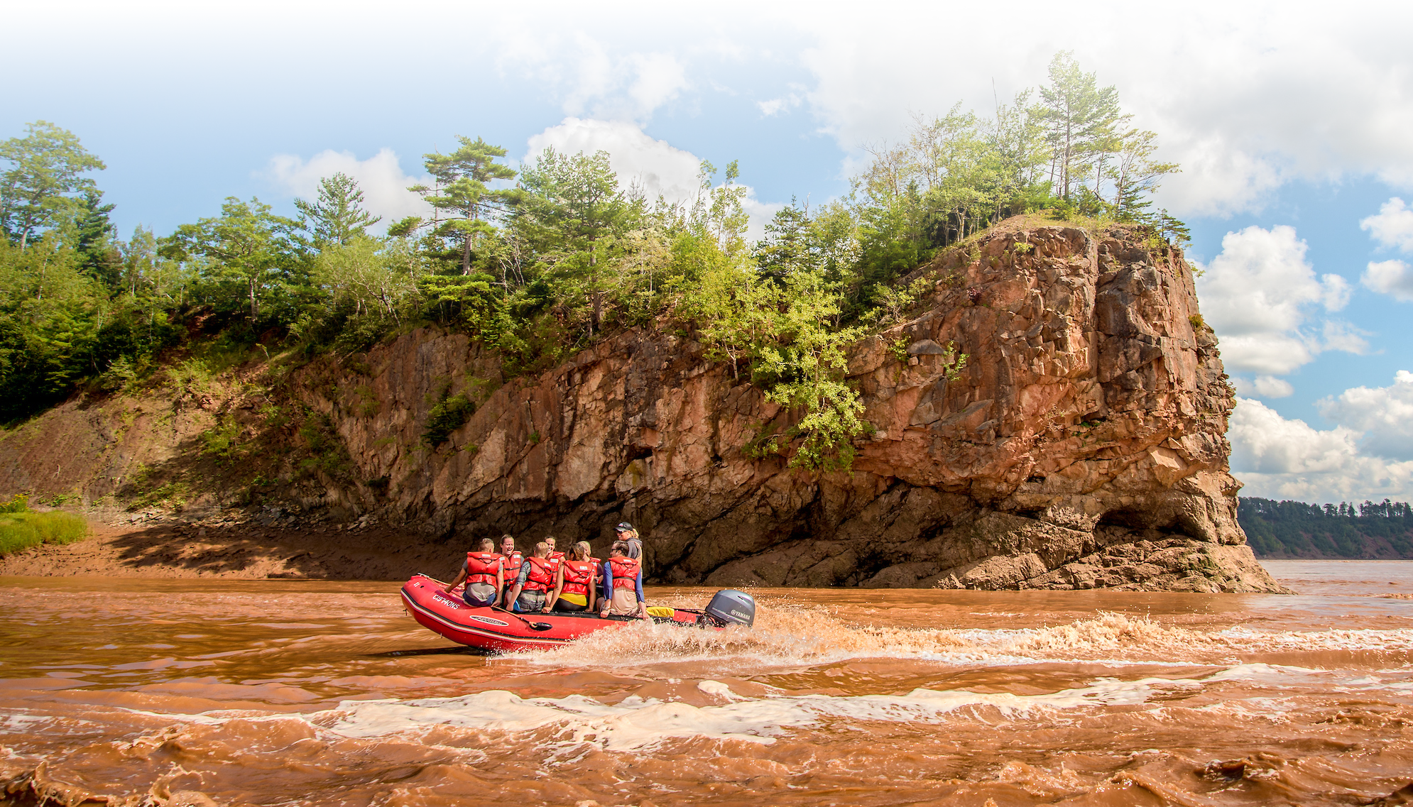 A zodiac boat carrying passengers travels down the Shubenacadie River for tidal bore rafting.