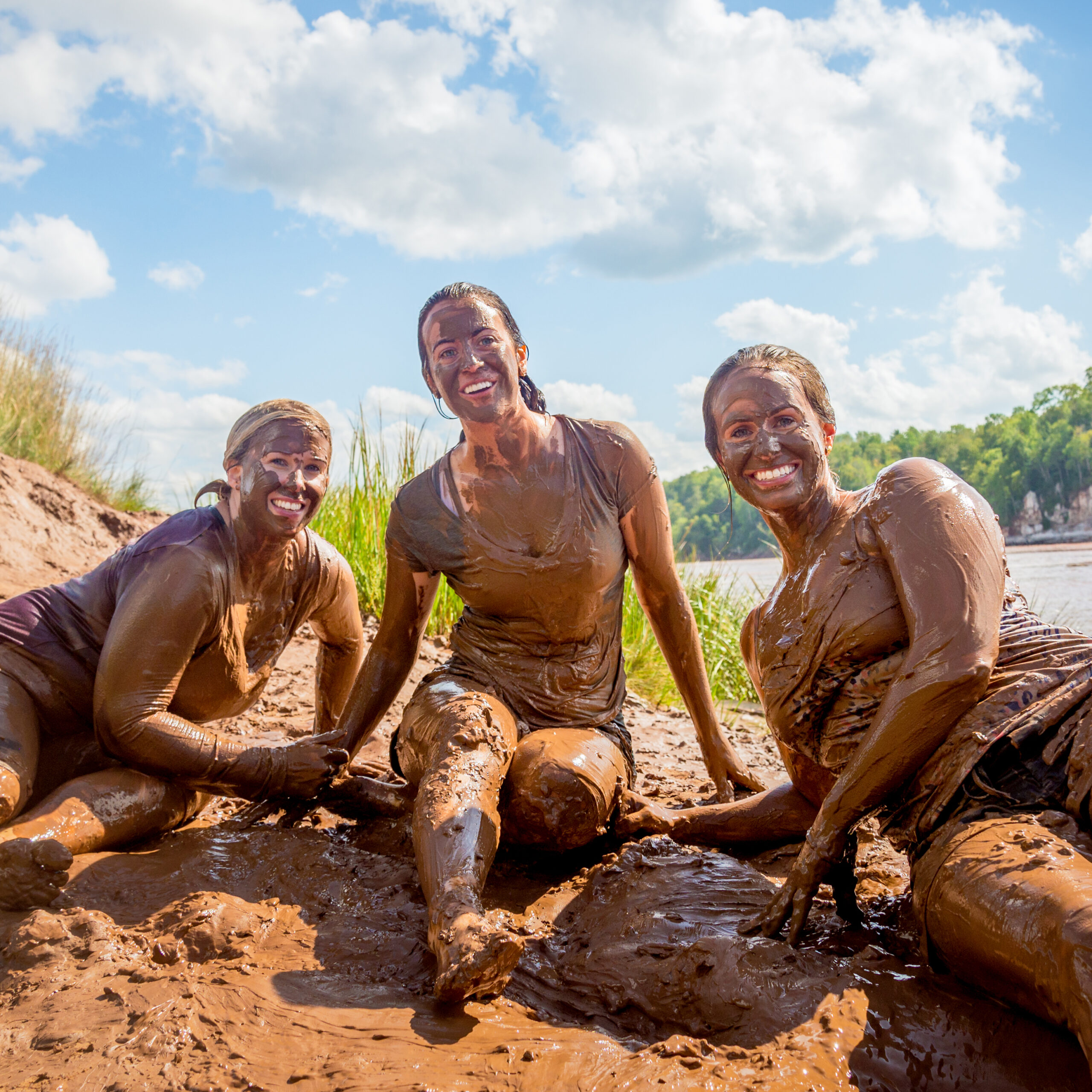 Three women covered in red mud from the Shubenacadie River pose for the camera after participating in mud sliding on their tidal bore rafting tour.