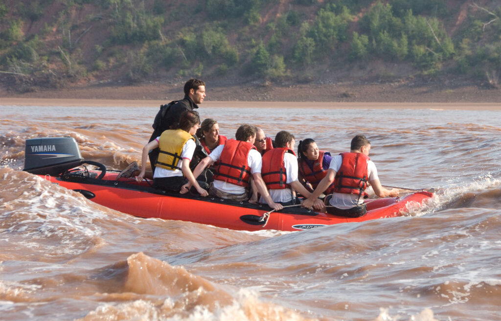 A zodiac raft carries passengers wearing life jackets through the rapids in the tidal bore.