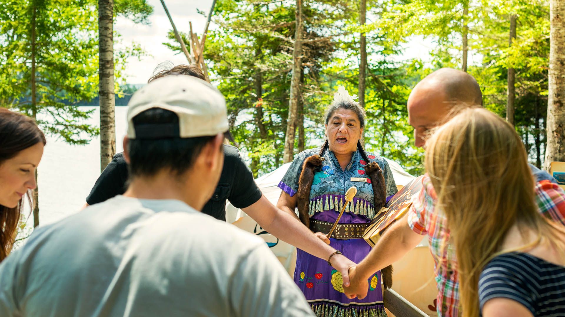 A Mi'kmaq woman dressed in regalia drums and signs for visitors during Eskasoni Cultural Journeys.