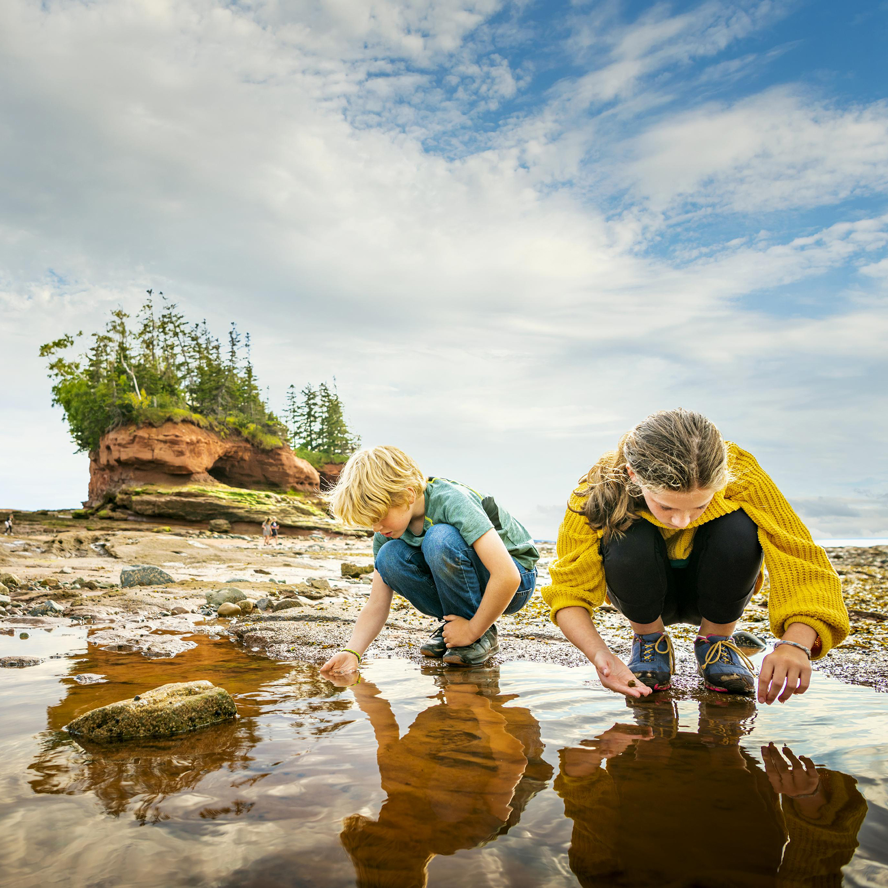 Two children exploring tide pools along the coast in Nova Scotia.