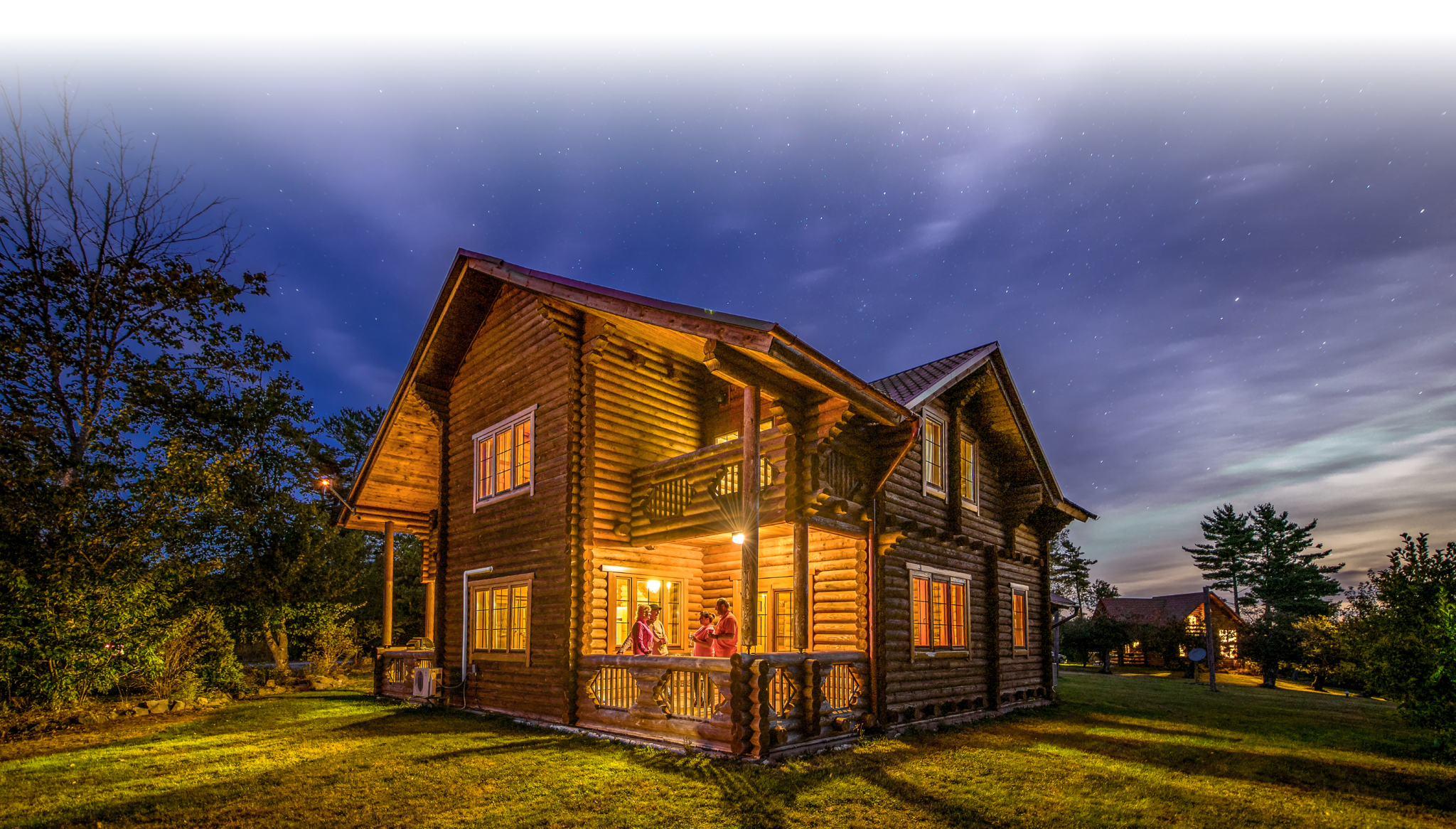 An image of the five bedroom cabin at Tidal Bore Rafting Resort lit up against the night sky with a group of people socializing on one of the outdoor decks.