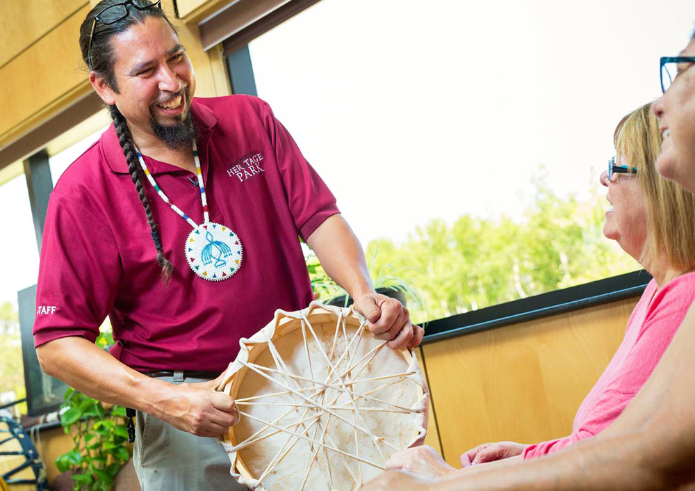 A Mi'kmaw man smiles as he shows a handmade drum to visitors at Membertou Heritage Park.