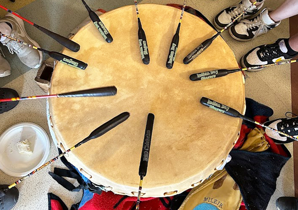 An overhead shot of multiple people drumming on a Mi'kmaq drum during a cultural experience.