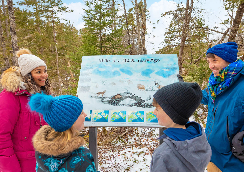 A family with two young children reads one of the interpretive signs along the Mi'kmawey Debert Interpretive Trail.